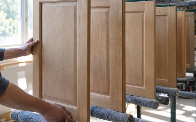 An unfinished wood door is lifted off a drying rack before priming.